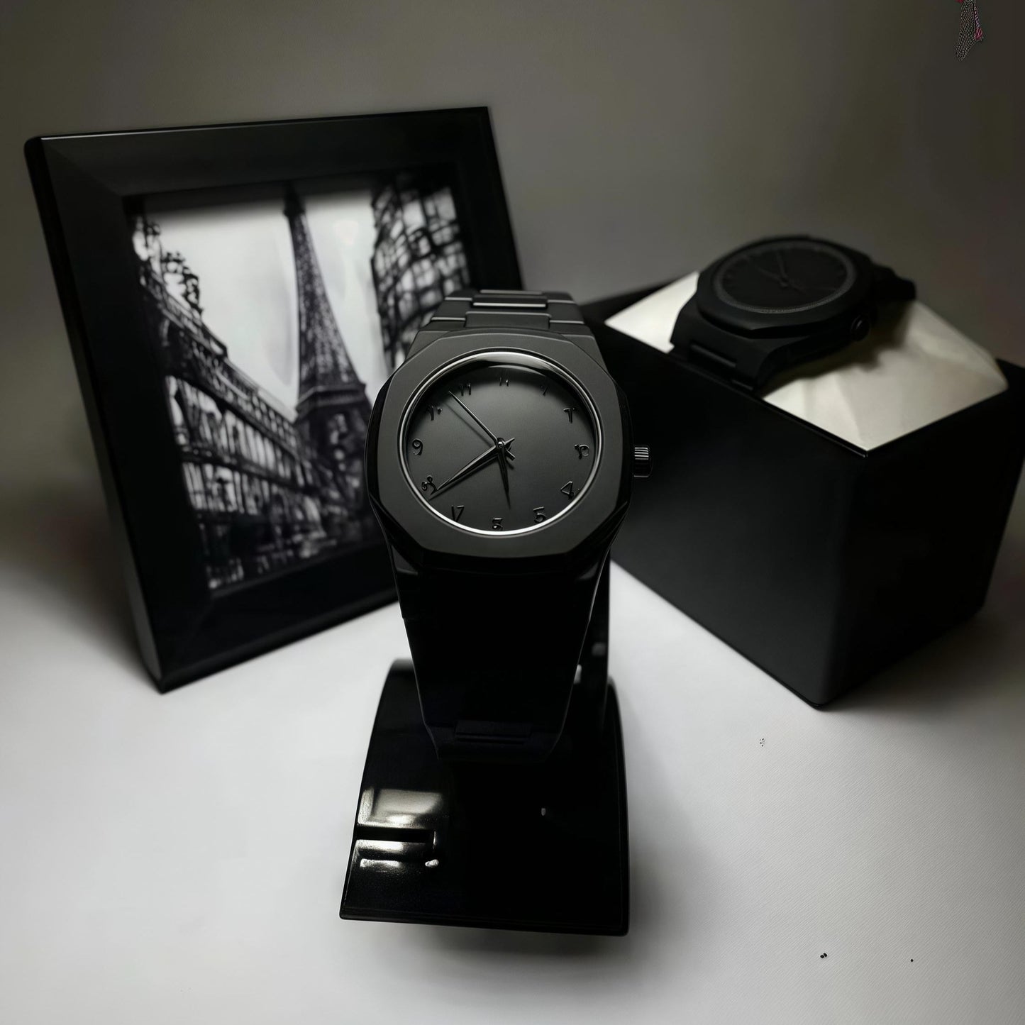Black clock on a stand with a black frame picture in the background