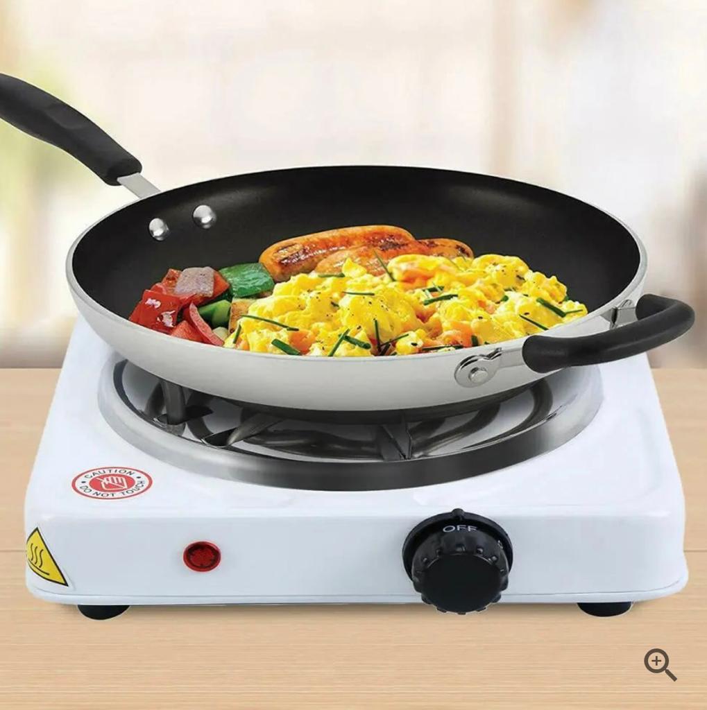 Single burner stove with a frying pan containing scrambled eggs, sausages, and vegetables on a wooden surface.