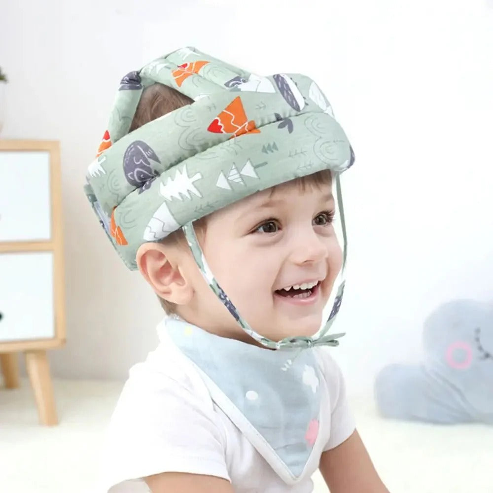 Child wearing a green helmet with cartoon designs, smiling indoors.