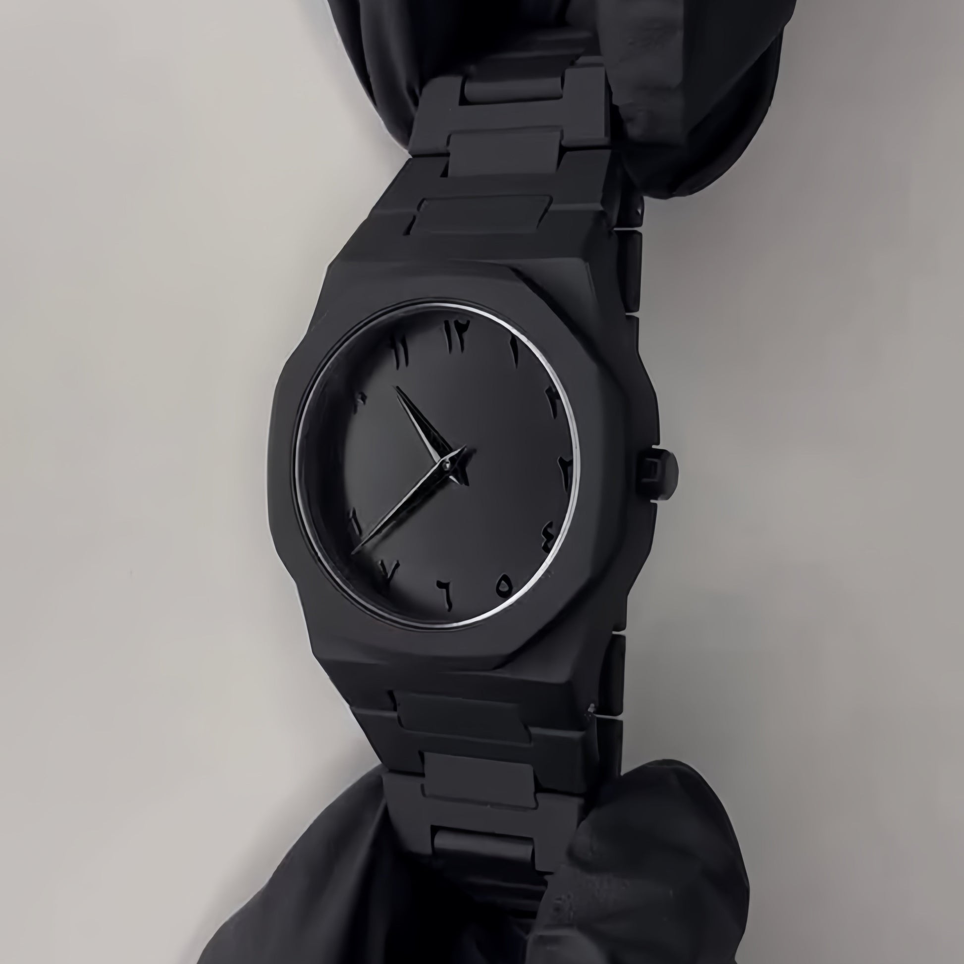 Black watch held by a gloved hand on a light gray background