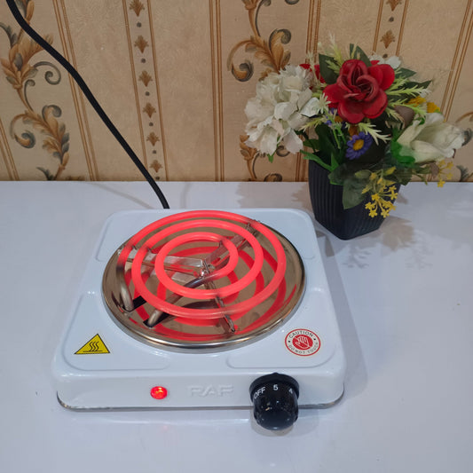 Small electric stove with red heating element on a table with floral arrangement in the background.